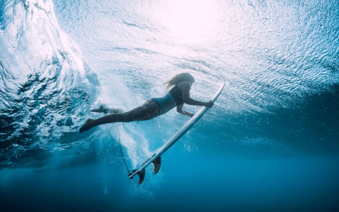 Wie du deinen Duck Dive verbessern kannst. Eine Frau taucht mit dem Surfbrett unter einer Welle durch.