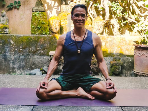 Yoga teacher Teddy Sun sitting on a yoga mat outside.